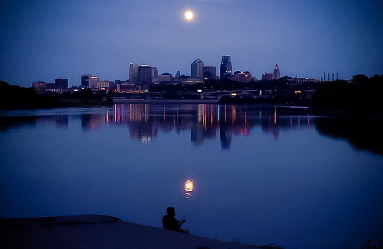 Một người đàn ông câu cá ở sông Missouri khi trăng tròn mọc lên phía trên đường chân trời của trung tâm thành phố Kansas City, Missouri.